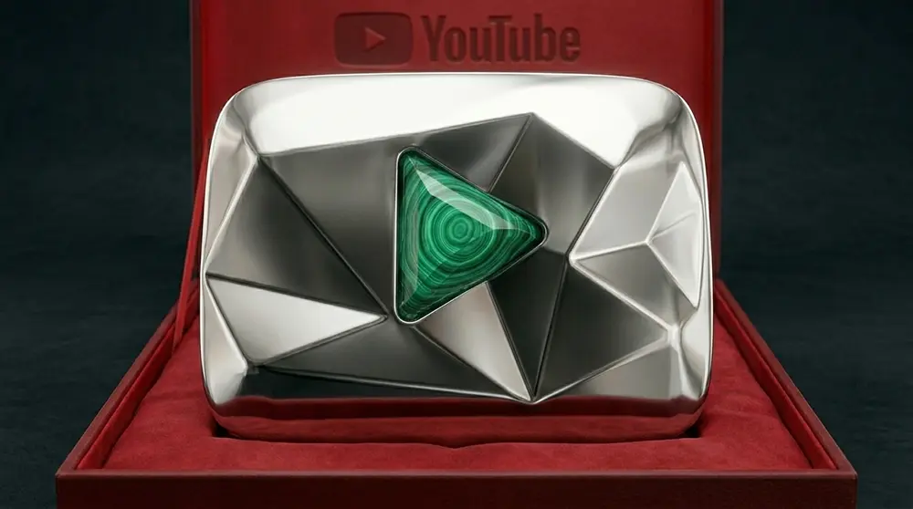 PROMPT: A dramatic product photograph showing three YouTube Tiger's Eye play button awards displayed in a row on a dark reflective surface. Each award features a heavy polished steel casing with a vivid yellow-orange crystal centrepiece shaped like the YouTube play button triangle. Warm amber-toned studio lighting from above creates golden reflections. Ultra-high detail commercial photography with a dark moody background.